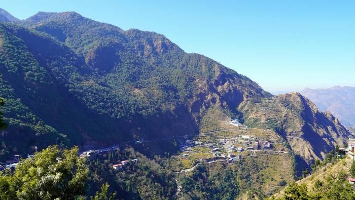 Distant mountain settlement nestled among lush green ridges under a clear azure sky