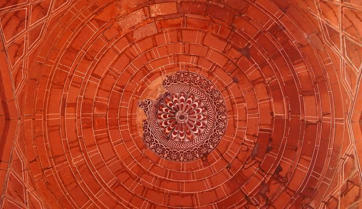 Detailed concentric design in red sandstone ceiling with floral centerpiece at Agra monument.