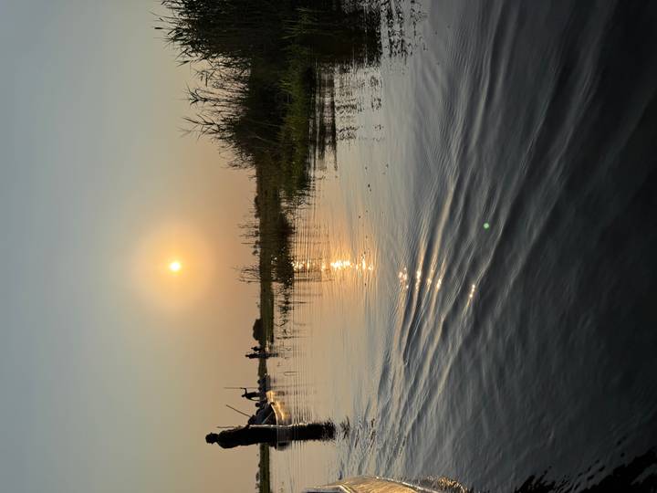 Low view of a calm water channel at sunset with orange sun reflecting on the ripples.