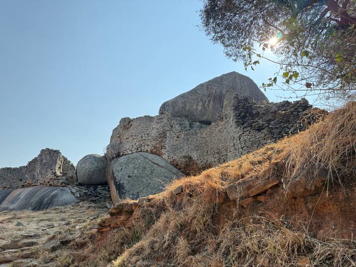 Ancient stone ruins and massive boulders on a hilltop under a bright blue sky.