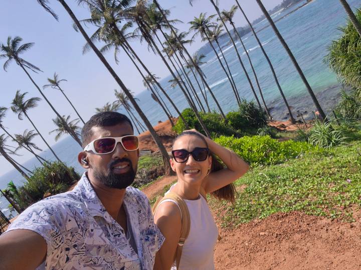 Cheerful couple take a selfie with leaning palm trees and blue Indian Ocean backdrop.