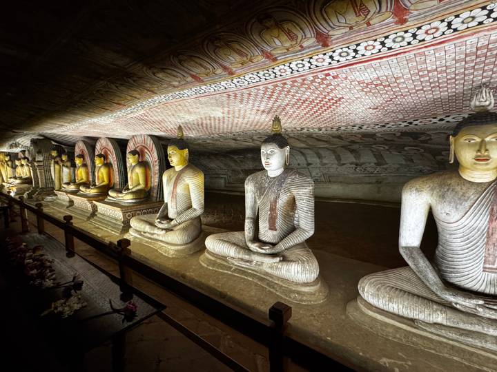 Row of illuminated Buddha statues lines the richly painted interior of Dambulla Cave Temple.