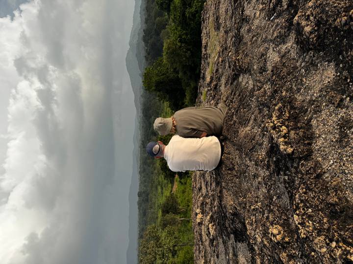 Couple sitting on a rocky outcrop admiring vast green landscape and rolling hills under moody sky