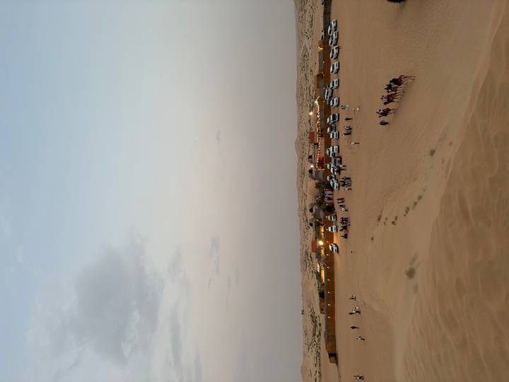 Wide desert scene of evening camp, 4x4s and camel caravan under fading light.