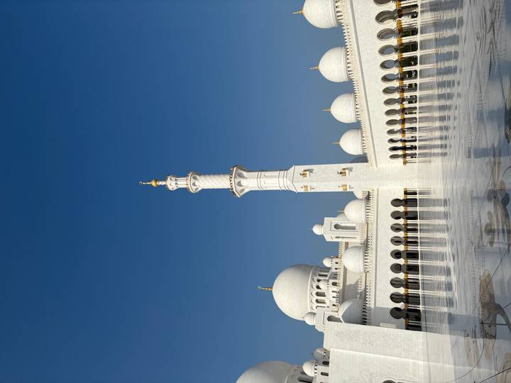Pristine white domes and minaret of Sheikh Zayed Grand Mosque against clear blue sky.