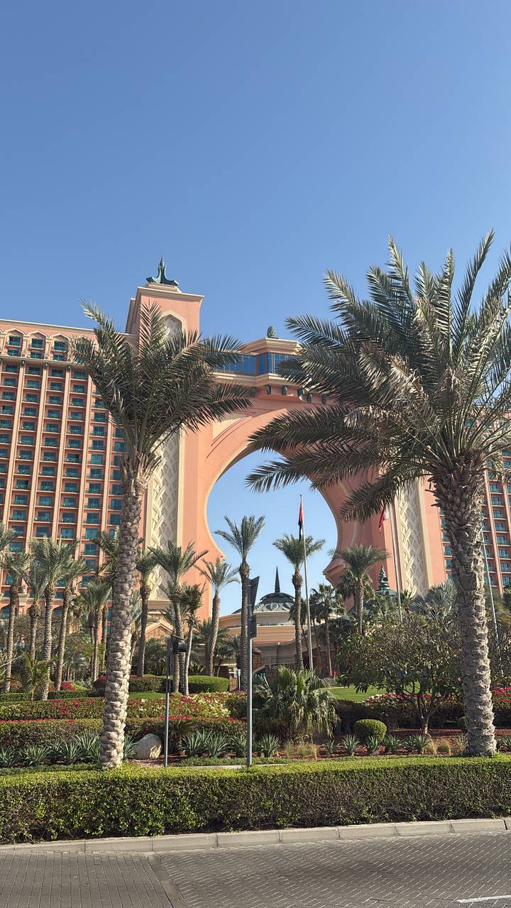 Iconic arch and palm-lined entrance of Atlantis resort framed by date palms.