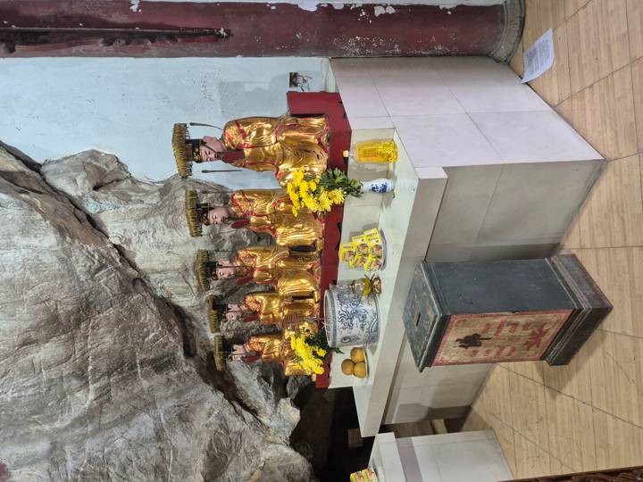 Row of gold-leaf statues inside a cave temple with offerings of flowers and fruit.