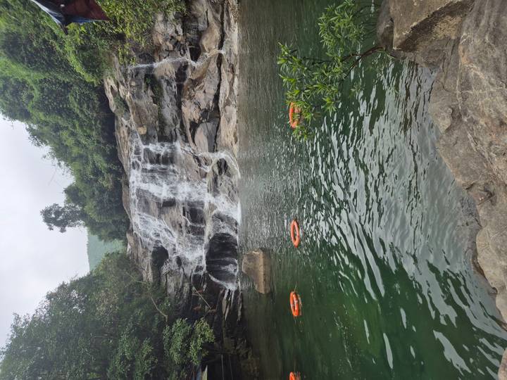 Small natural waterfall cascading into a green pool with flotation rings floating on the surface.