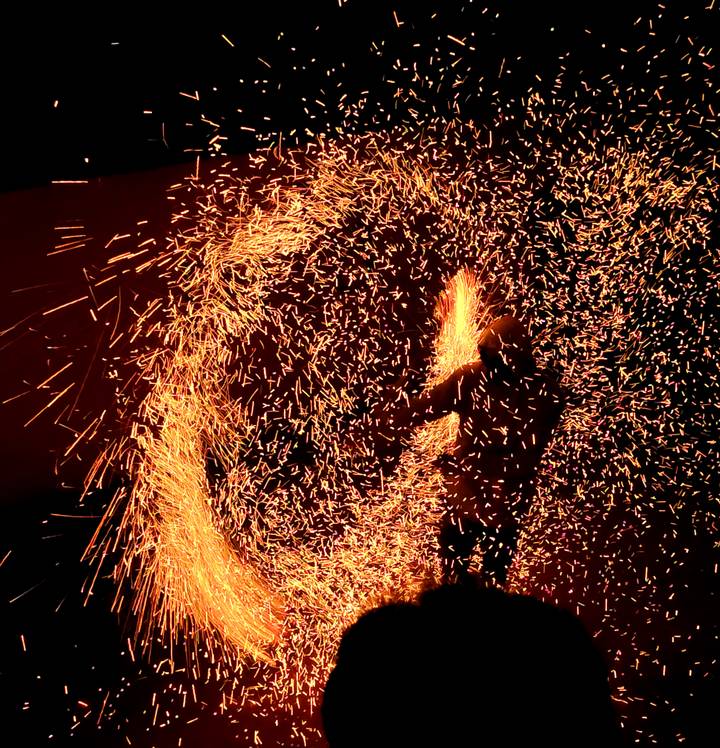 Performer spins fire, creating a dramatic swirl of golden sparks against the night sky.