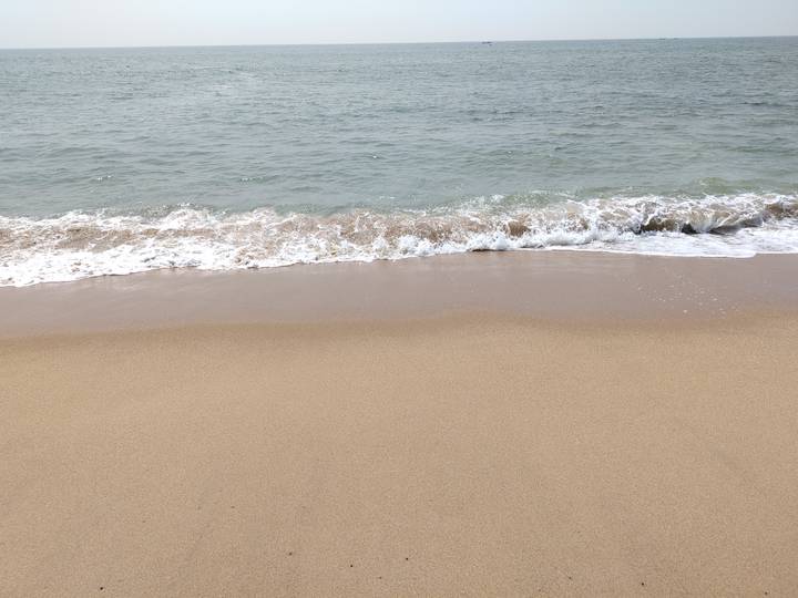 Gentle wave laps onto a quiet sandy beach under an overcast sky.