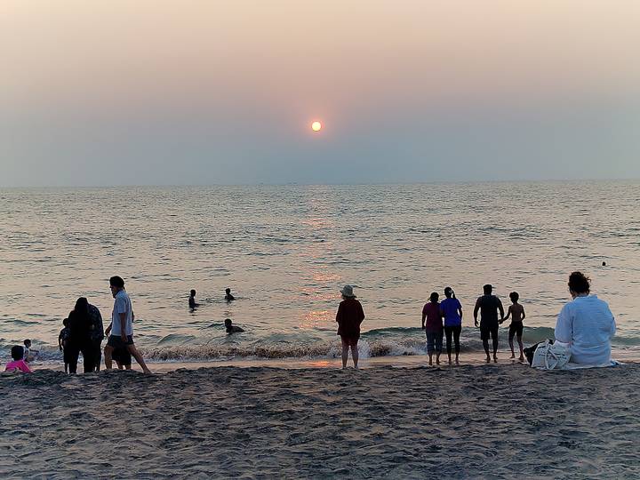 People wade and watch the sun set over the Arabian Sea from a sandy Kerala beach.