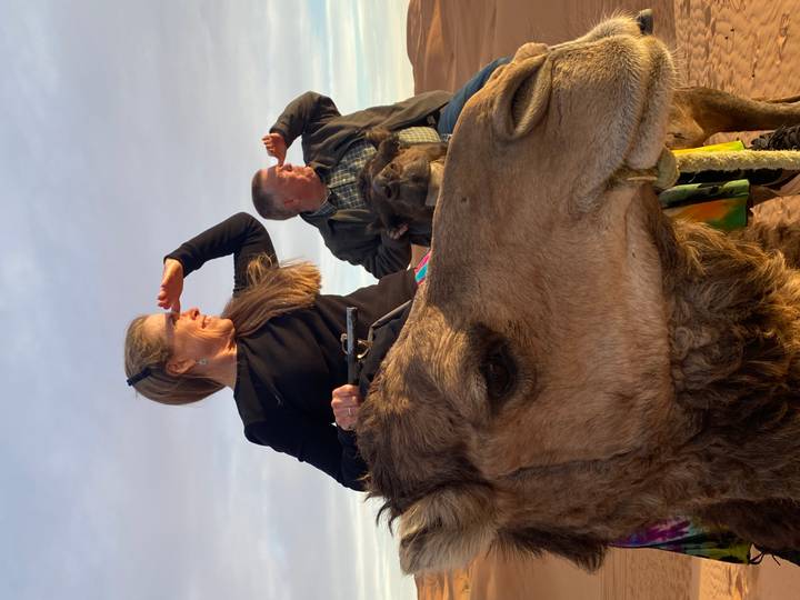 Couple riding camels in the Sahara scans the horizon under warm evening light.