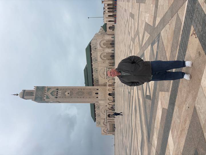 Visitor stands before the grand Hassan II Mosque with its soaring minaret under cloudy skies.