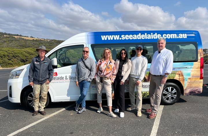 Tour group poses beside branded minibus on a coastal Australian road