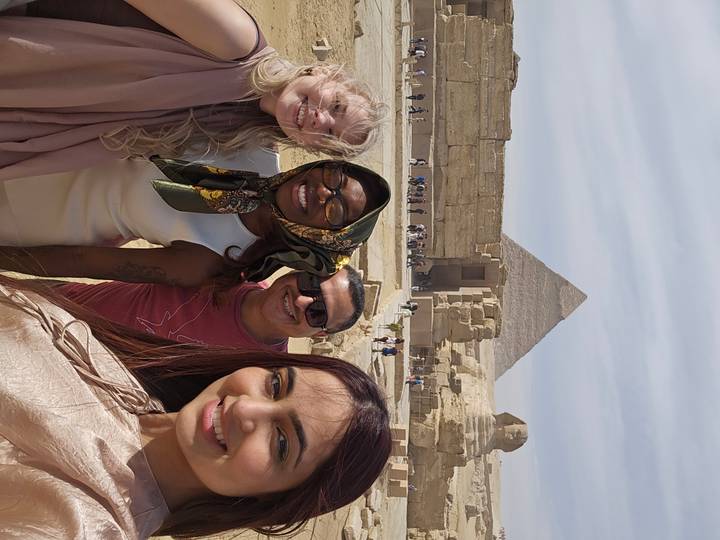 Four smiling travellers take a selfie with the Great Pyramid and Sphinx in the background.