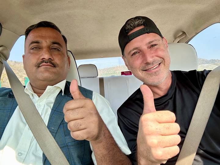 Two men inside a car giving thumbs-up while wearing seatbelts.