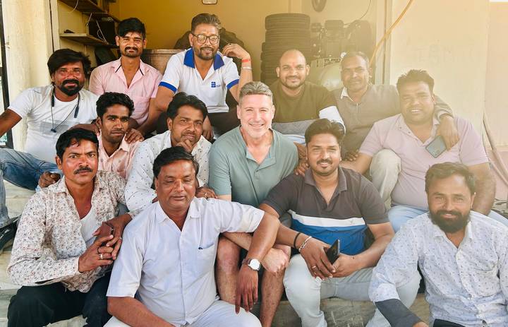Large group of mechanics and a visitor smiling together in a workshop setting.