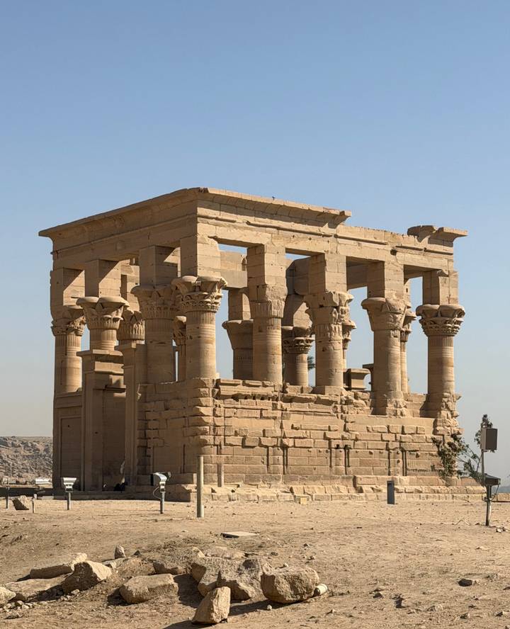 Elegant stone kiosk with papyrus-style columns on Philae Island against blue sky.