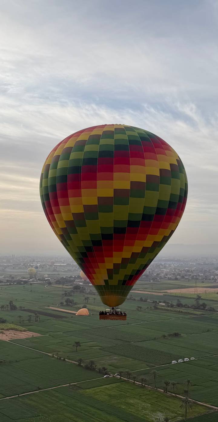 Colorful hot-air balloon floating above hazy landscape at dawn.