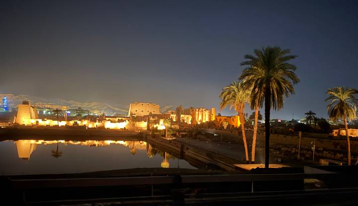 Illuminated ruins of Luxor Temple reflected in the Nile River at night.