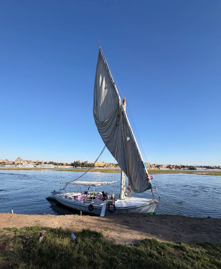 Traditional felucca sailboat gliding on the Nile with crew beneath a billowing sail.
