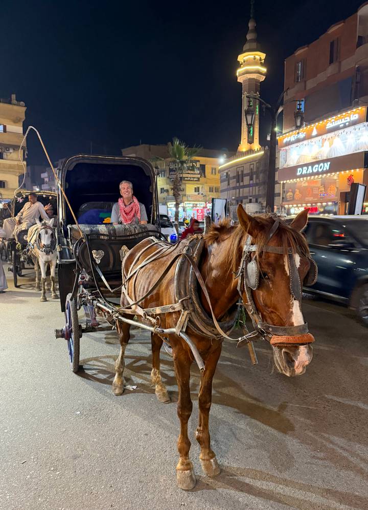 Traveler riding a horse-drawn carriage through a lively city street at night.