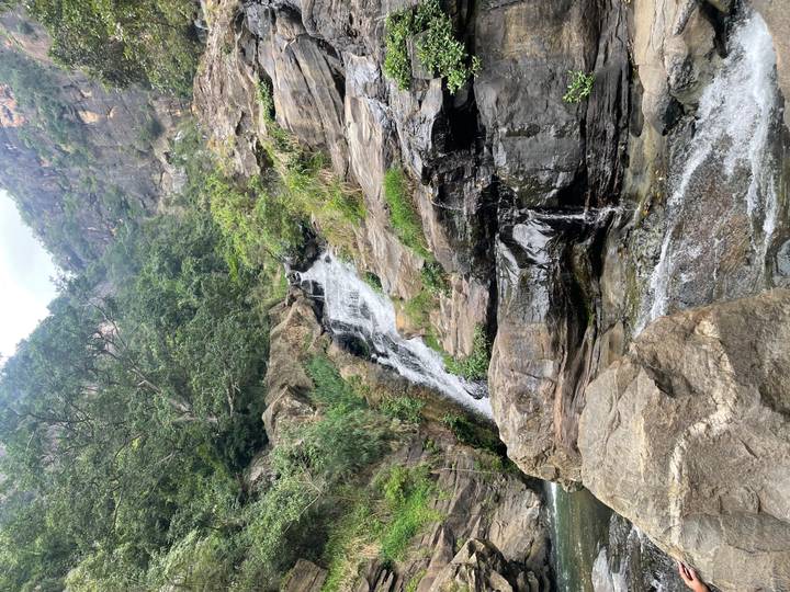Rocky waterfall cascading through lush green forested gorge.