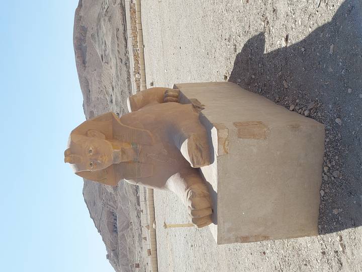 Daytime view of a weathered sandstone sphinx against barren desert hills.