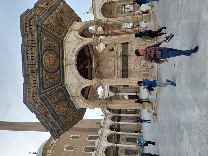 Visitors browse the marble courtyard and ornate ablution fountain of a grand Ottoman mosque.