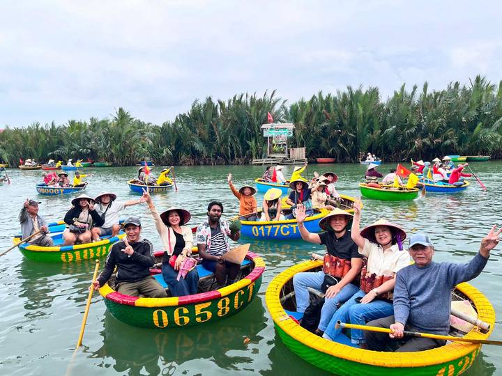 Dozens of tourists in brightly painted basket boats wave while floating on a palm-lined river.