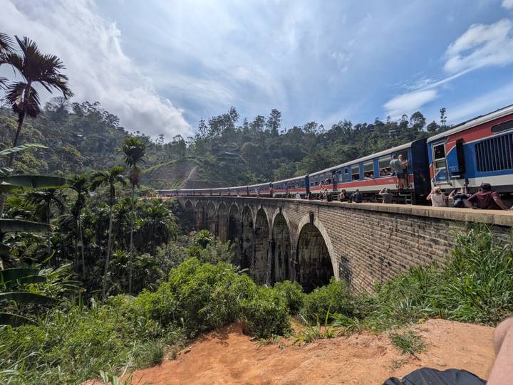 Long passenger train crossing the famous stone Nine Arches Bridge above a lush green valley.