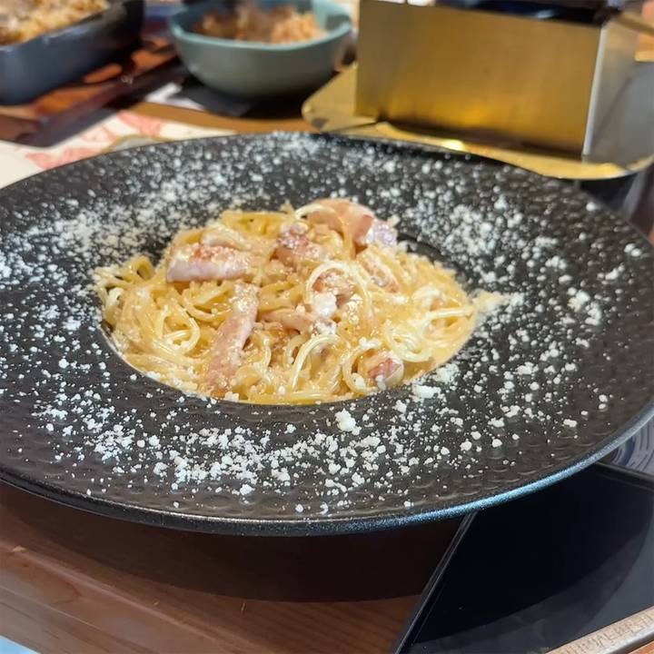 Plate of creamy carbonara pasta sprinkled with grated cheese served on a dark ceramic dish.