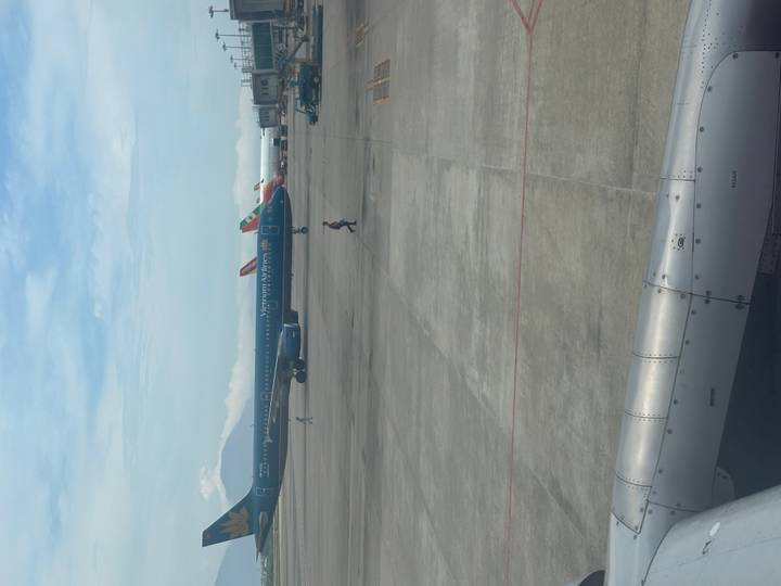 Vietnam Airlines jet parked on an airport apron with other aircraft and distant mountains.
