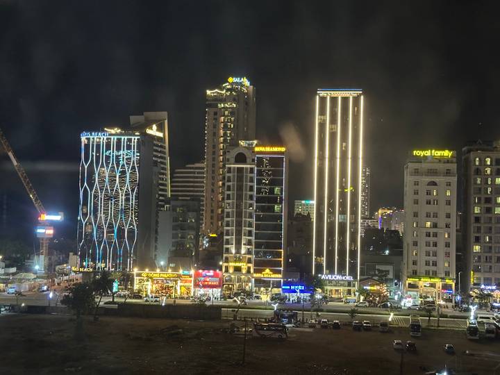 Modern city skyline illuminated at night with brightly lit high-rise buildings and street activity below.