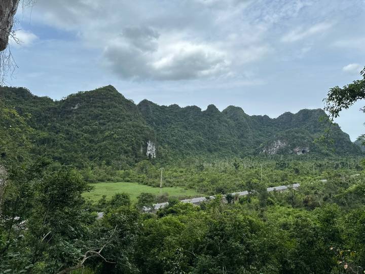 Dense green karst hills rising behind a valley road under a partly cloudy sky.