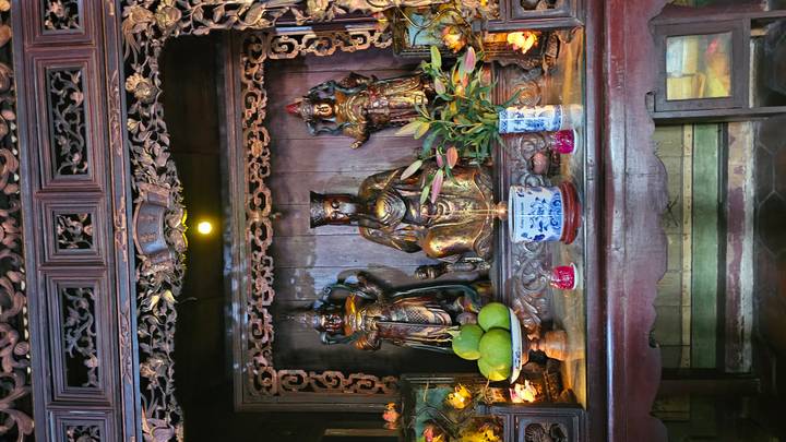 Elaborate wooden altar with bronze deities, fruit offerings and soft interior lighting.