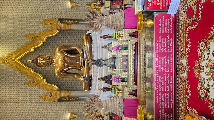 Gleaming Golden Buddha statue enthroned within an ornate Thai temple hall.