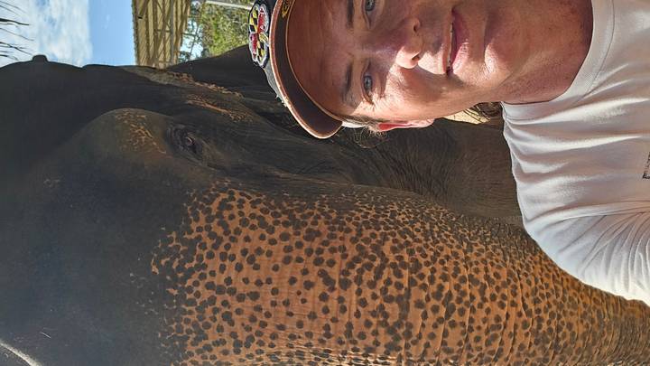 Close-up selfie with half of an elephant’s head beside a smiling traveler.