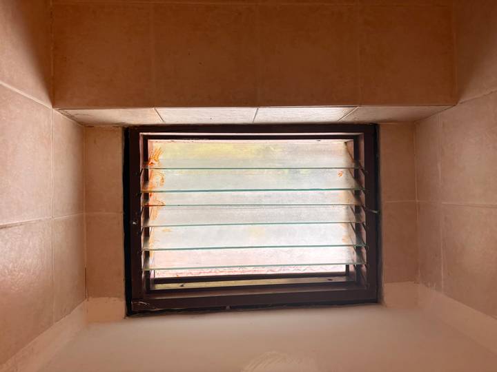 Small bathroom window with frosted glass and rust stains in tiled wall.