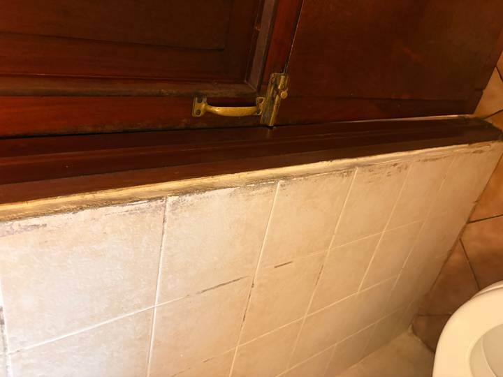 Moldy door frame beside tiled bathroom wall and brass handle.