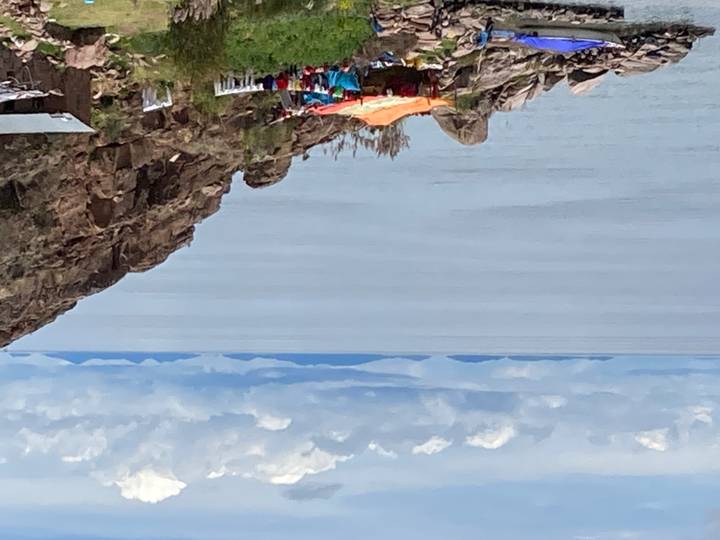 Calm expanse of Lake Titicaca with distant islands and colorful tarp shelter on rocky shore.