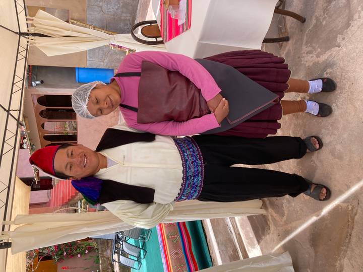 Local hosts in traditional Taquile Island attire smile under event canopy.