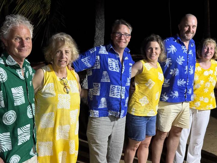 Smiling tour group wearing matching patterned shirts poses at night under palm trees.