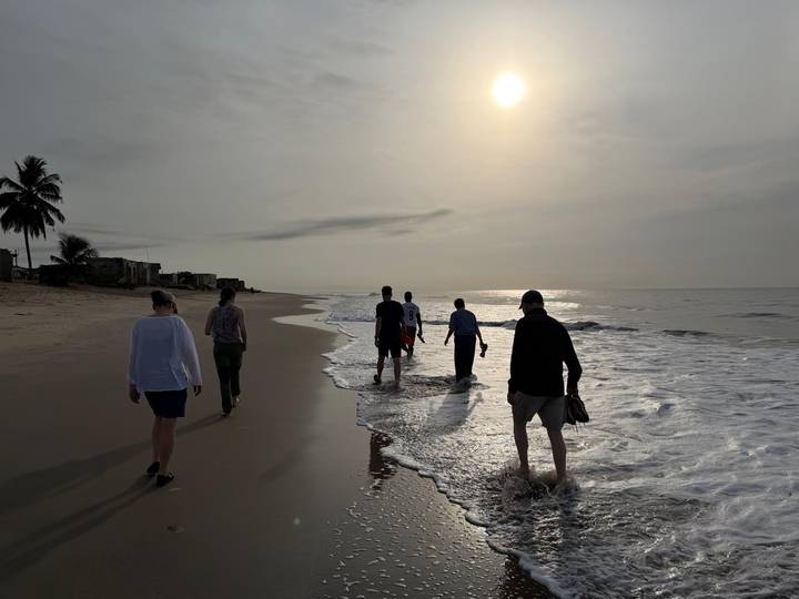 Travelers stroll along quiet beach shoreline in soft morning sunlight.