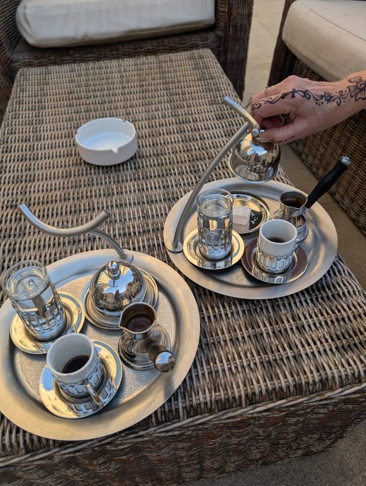Traditional coffee service with small cups, glasses of water and sugar cube on silver trays.