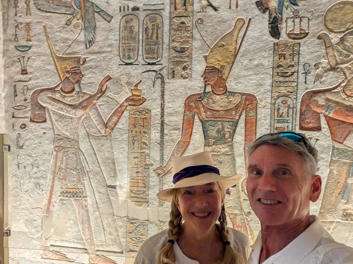 Selfie of two travellers standing before vivid wall reliefs inside an ancient Egyptian temple.