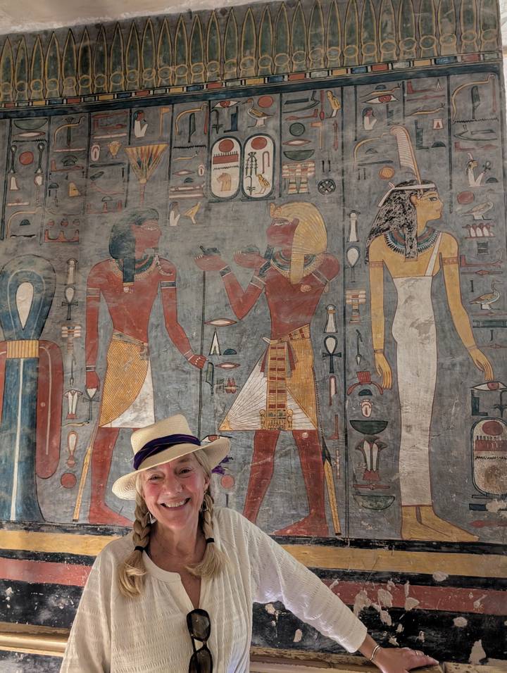Visitor wearing a hat stands beneath colourful wall paintings inside a tomb in the Valley of the Kings.