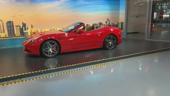 Red Ferrari convertible displayed indoors against a printed Abu Dhabi skyline backdrop.