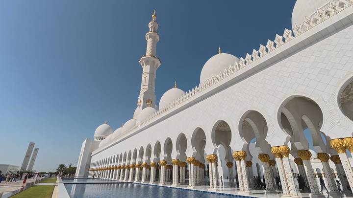 Side perspective of Sheikh Zayed Grand Mosque with reflective pools and gilded columns.