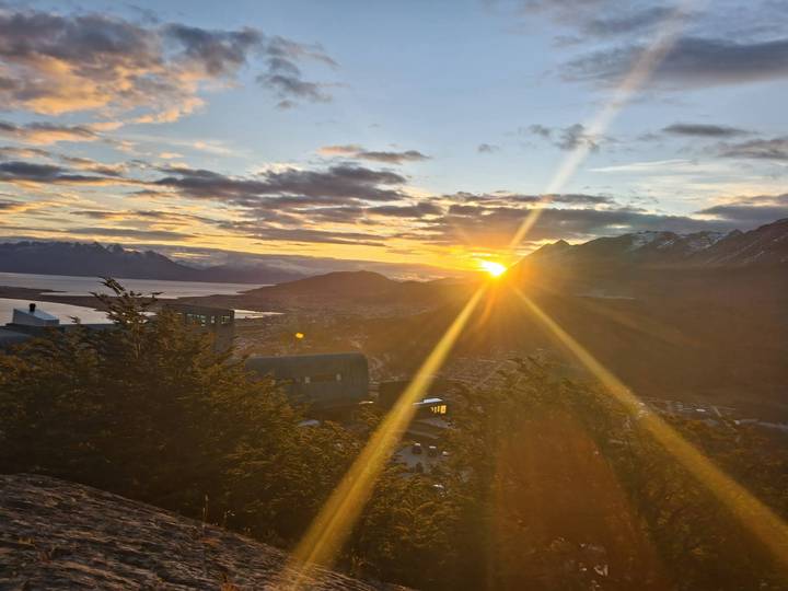 Dramatic sunset over Ushuaia with golden rays streaming across mountains and the Beagle Channel.